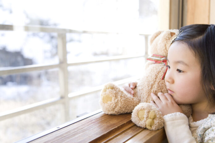Girl looking outside from the window, holding teddy bear